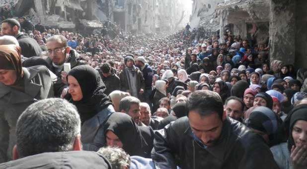 Syrian refugees wait in line in Damascus for bags of food.