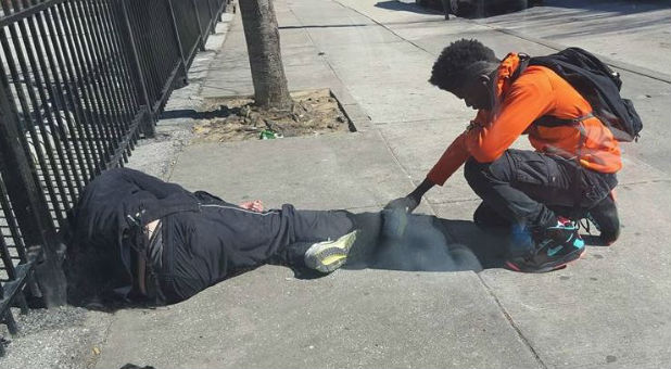 A boy prays over a homeless man.