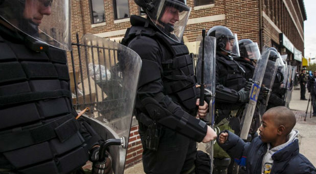 A young boy greets police officers in riot gear during a march in Baltimore, Maryland May 1, 2015 following the decision to charge six Baltimore police officers -- including one with murder -- in the death of Freddie Gray, a black man who was arrested and suffered a fatal neck injury while riding in a moving police van/