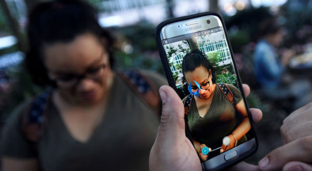 A Pokemon appears on the screen next to a woman as a man plays the augmented reality mobile game