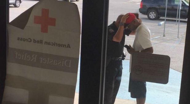 This photo was taken after the Red Cross told the police captain he could not pray inside the shelter. The man he is praying with lost his home in the flood.