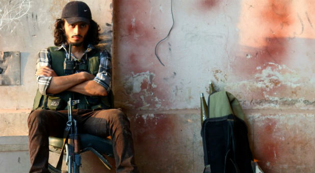 A rebel fighter sits with his weapon in the artillery academy of Aleppo, Syria