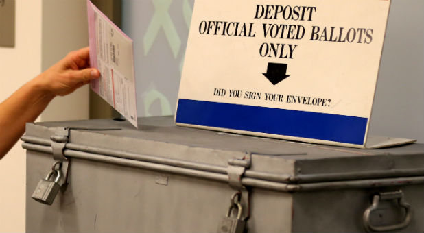 A ballot is placed into a locked ballot box by a poll worker as people line-up to vote early at the San Diego County Elections Office in San Diego, California, U.S.