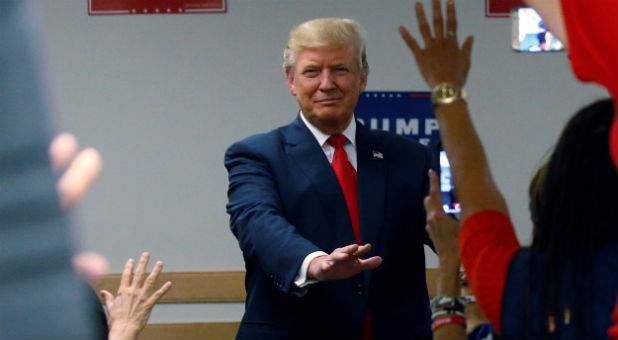 Donald Trump holds his hands out in prayer as people at a phone bank pray for him before a campaign rally.