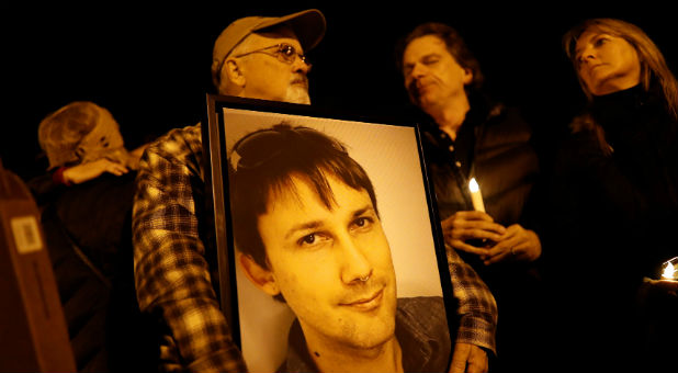 Brian Hough holds a photograph of his son Travis, who was among the deceased at the warehouse fire, during a vigil in Oakland.