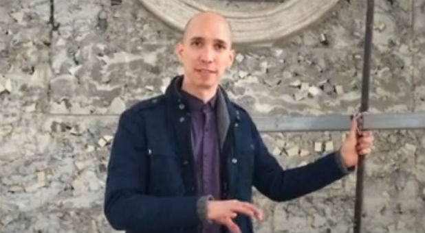 A man stands by a handmade cross and explains its backstory.