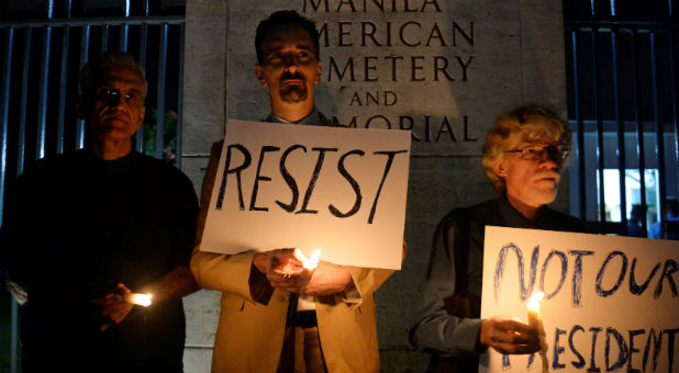 U.S. citizens Omar Tiwana, Tim Ortiz and Donald Goertzen light candles while holding up placards during a protest ahead of U.S. President-elect Donald Trump's inauguration