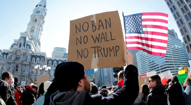 Protester Brandon McTear holds a sign and the American fag as demonstrators gather to protest against U.S President Donald Trump in Philadelphia