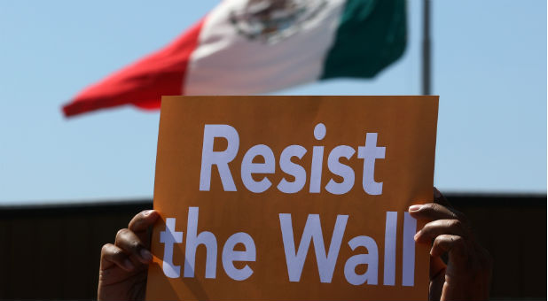 A Mexican flag in Tijuana is seen behind an immigrant-rights protester near the U.S.-Mexico border wall in San Ysidro, a district of San Diego