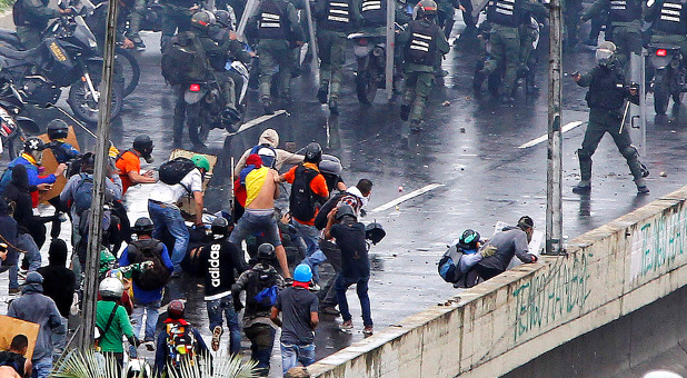 A member of the riot security forces (R) points what appears to be a pistol towards a crowd of demonstrators during a rally against Venezuela’s President Nicolas Maduro’s government in Caracas, Venezuela.