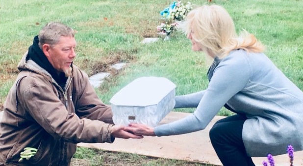 Linda Znachko, right, hands a man the casket as they prepare to bury a child.