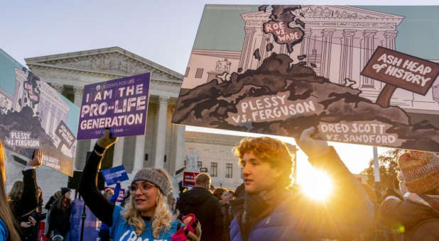 Anti-abortion protesters bear signs that read