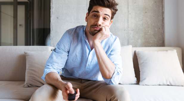 Bored man sitting on couch holding TV remote