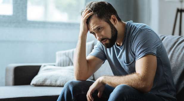 Man sitting with one hand on forehead, looking sad and gloomy