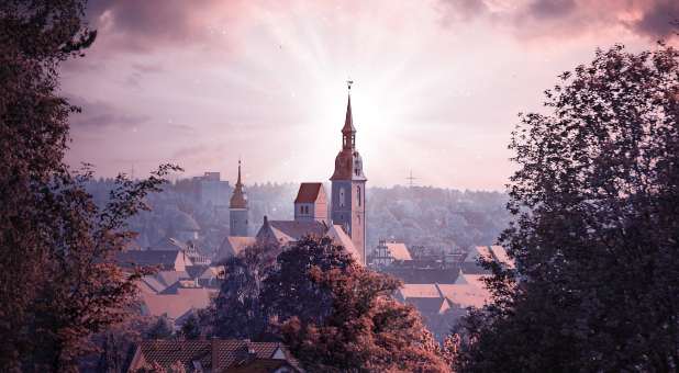 Chuch above city with glow of sun around steeple