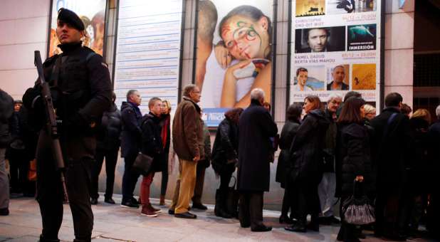 A man stands guard while people pay their respects to Charlie Hebdo victims.