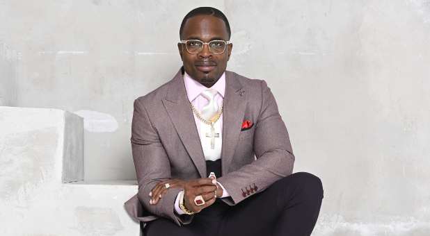 Bishop Lamor M. Whitehead wearing tuxedo with large silver cross on heavy chain, large rings.