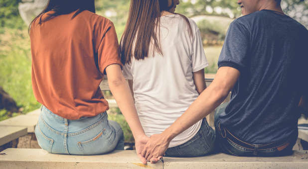 A man holding hands with a woman out of his wife's sight.